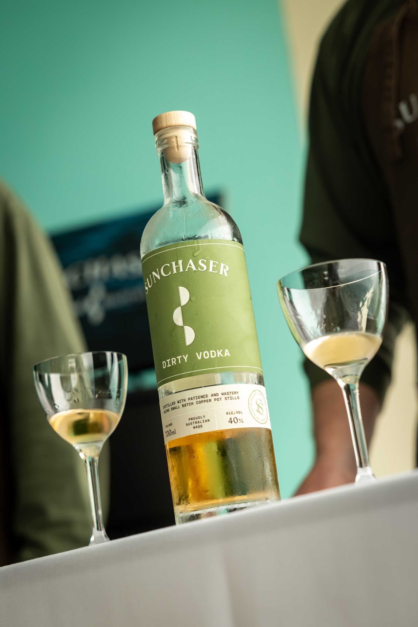 Two martini glasses beside a bottle of Sunchaser Dirty Vodka at a tasting event.