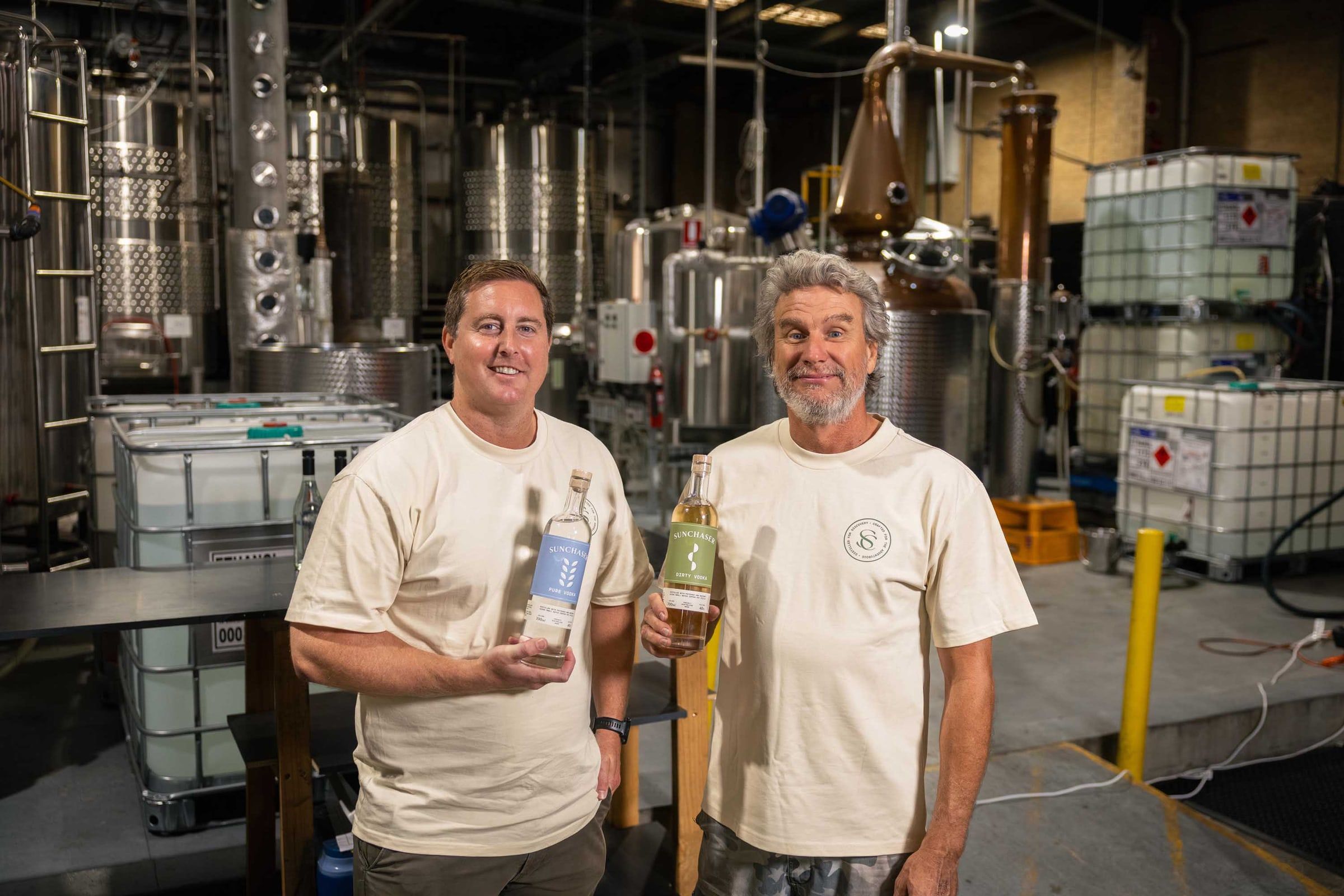 The two Sunchaser founders holding bottles of Pure and Dirty Vodka in the distillery.