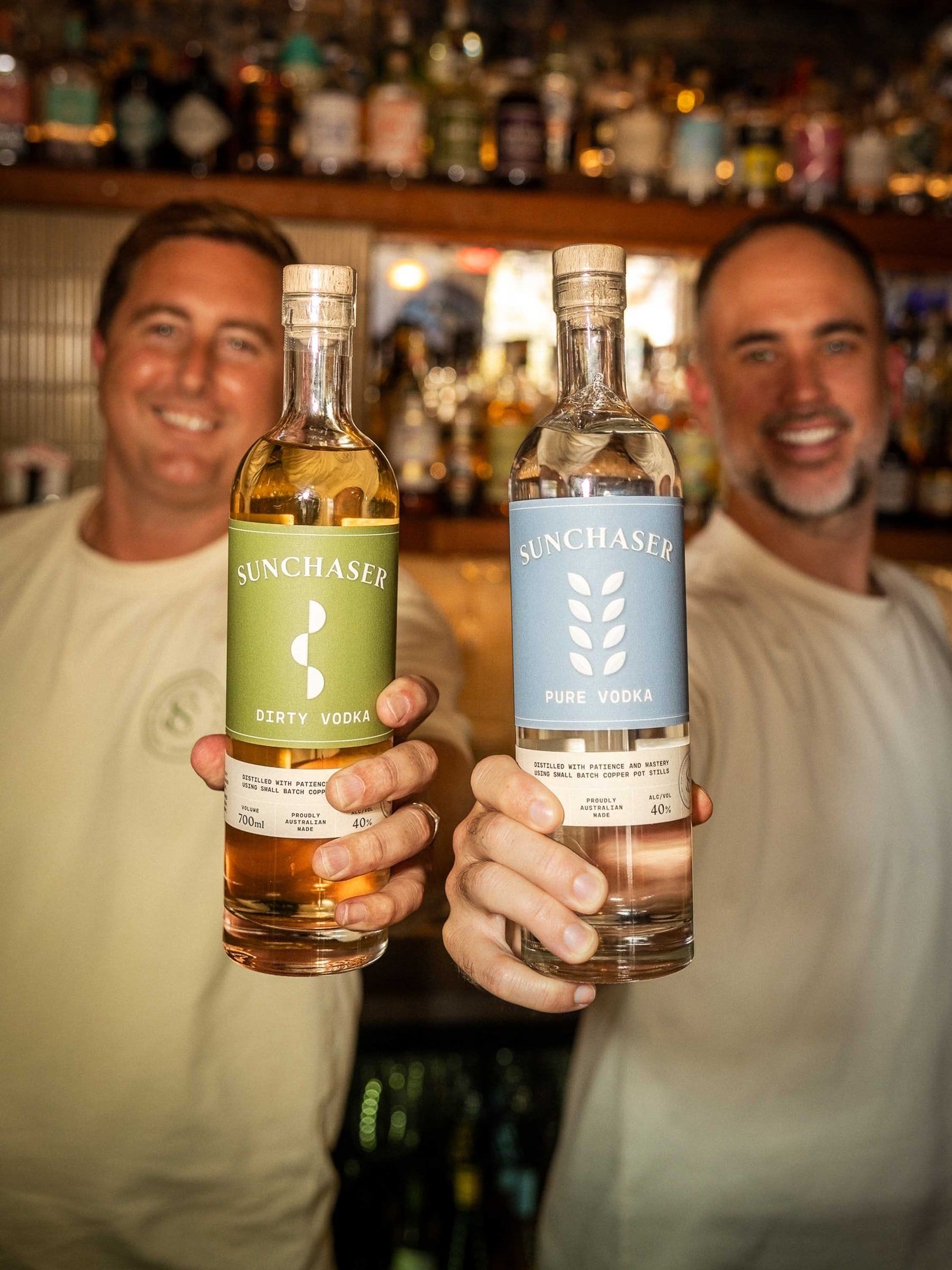 The founders smiling and holding up bottles of Dirty and Pure Vodka.
