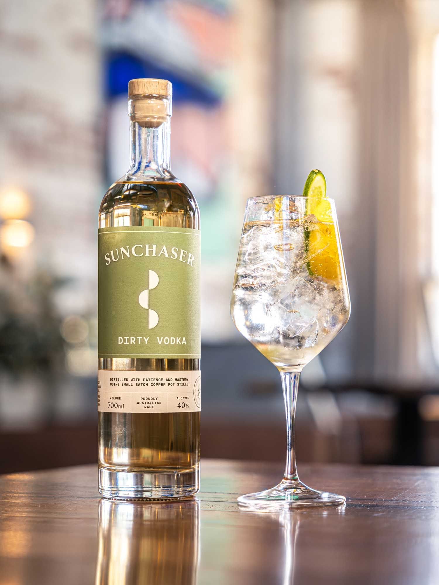 A Dirty Spritz in a wine glass with ice and citrus beside a bottle of Sunchaser Dirty Vodka.
